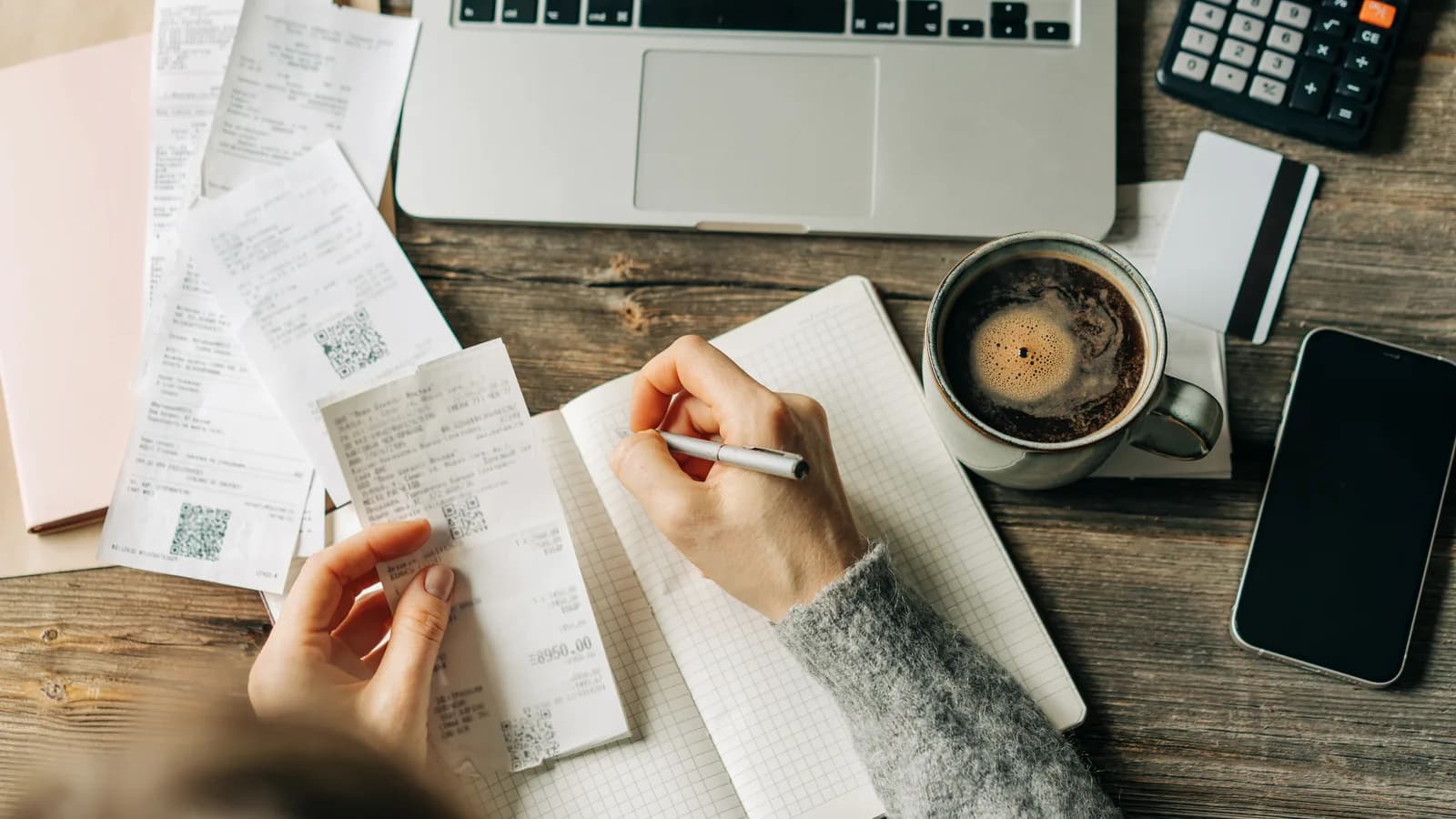 An accountant working through a stack of paper receipts beside a laptop, calculator and notebook